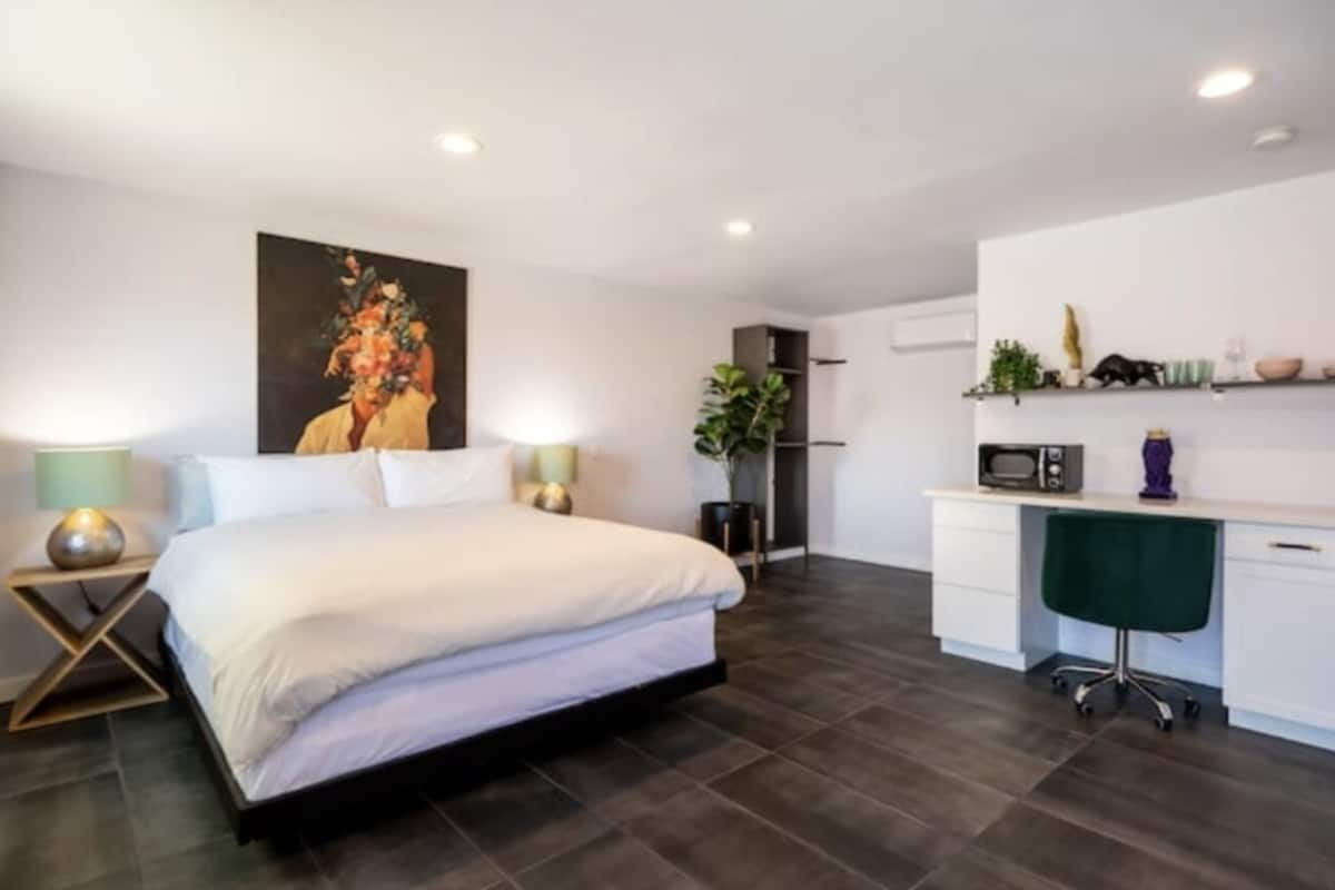A modern bedroom with a large bed, bedside tables, a desk, and a chair.