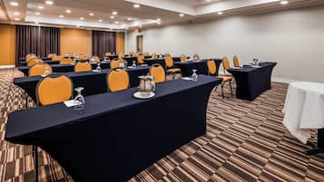 Un salón de conferencias con filas de mesas, sillas y jarras de agua.