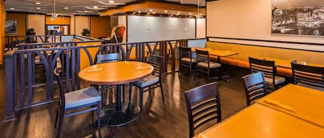 A restaurant interior with round tables, booths, and a high ceiling with recessed lighting.