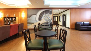 Un hall con una mesa central y sillas, una estantería, un sofá y un gran mural en la pared.