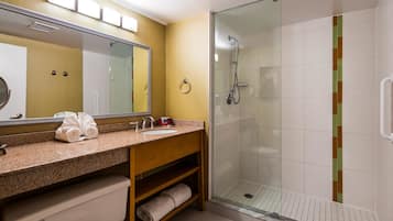 Un baño moderno con encimera de granito, un espejo grande, cabina de ducha con paredes de vidrio y un perchero para toallas.