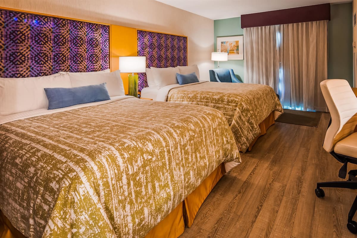 A hotel room with two beds, a desk, and a chair.