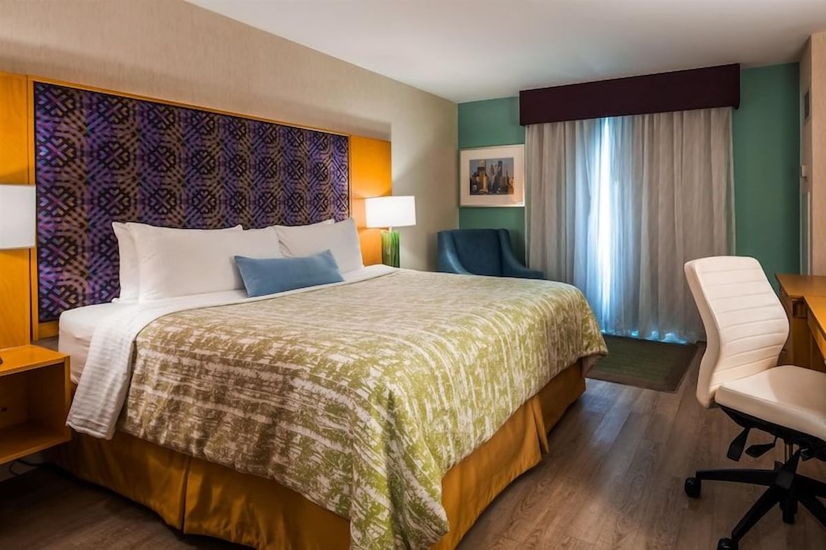Una habitación de hotel con cama, escritorio, silla, televisor y ventana con cortinas.
