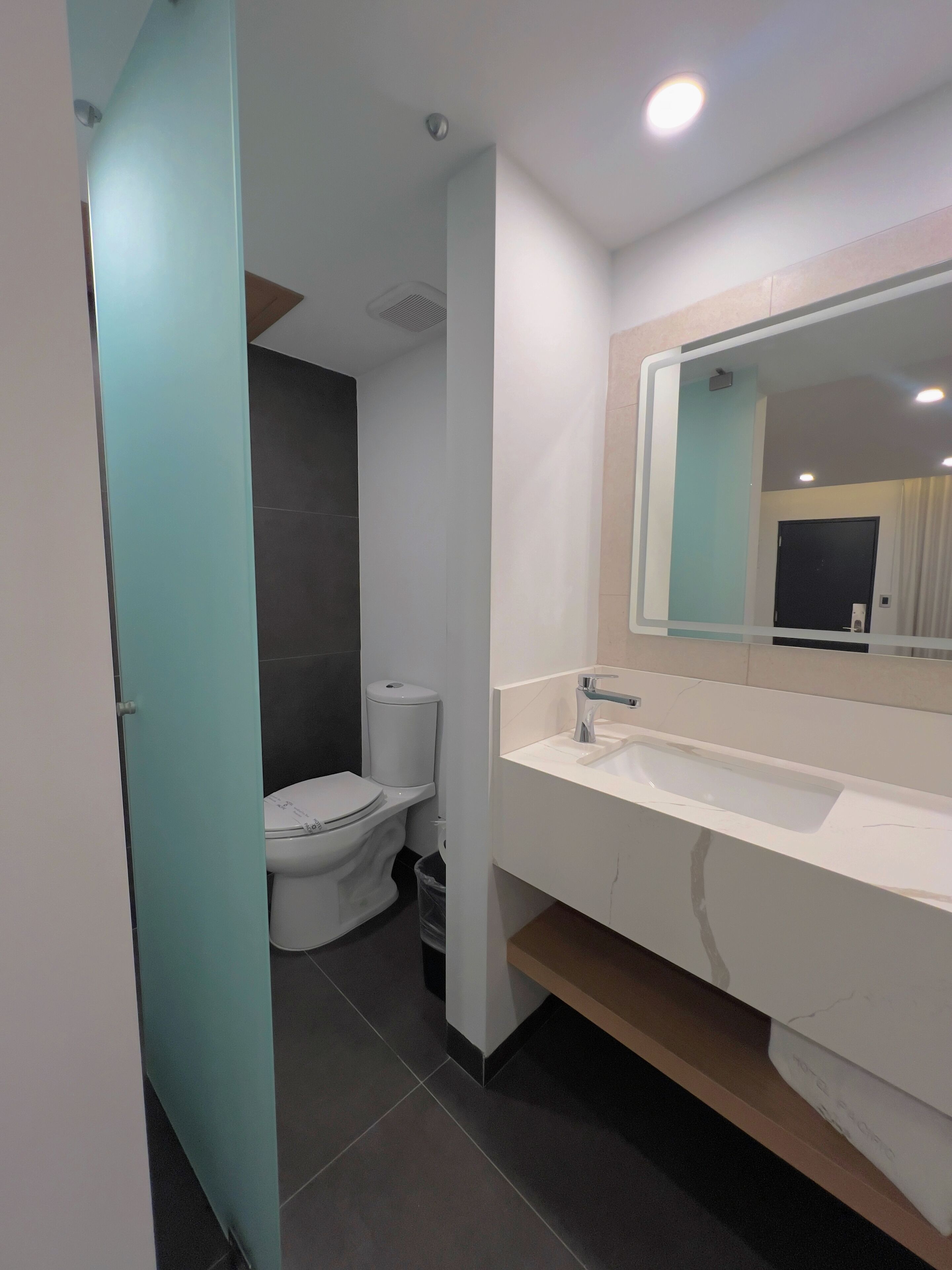 Un baño moderno con inodoro blanco, lavamanos con espejo y una puerta azul claro.