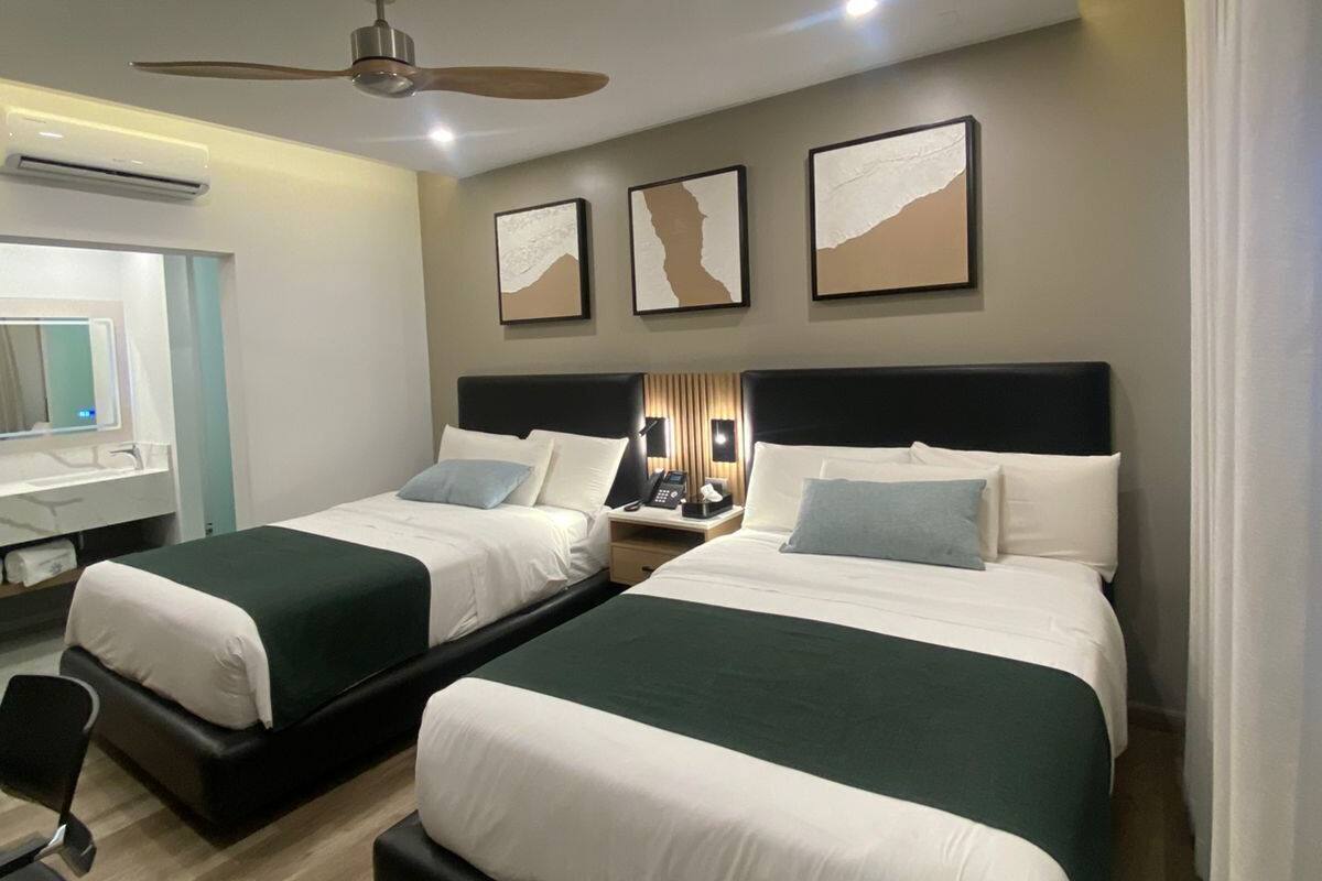 A hotel room with two beds, a desk, and a chair. There is a ceiling fan and wall-mounted artwork.