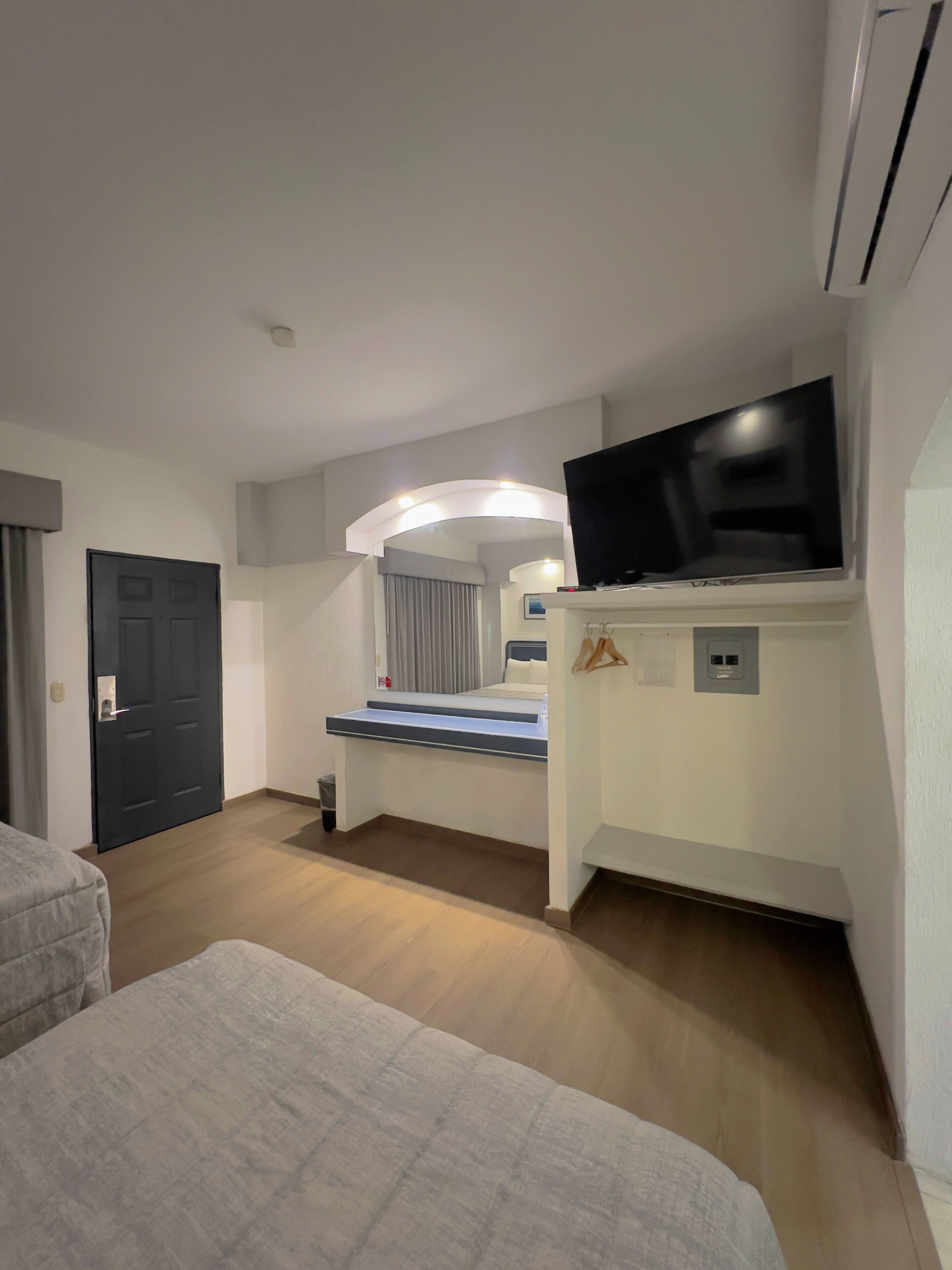 Ett hotellrum med en säng, en tv på ett stativ, ett skrivbord och en spegel.