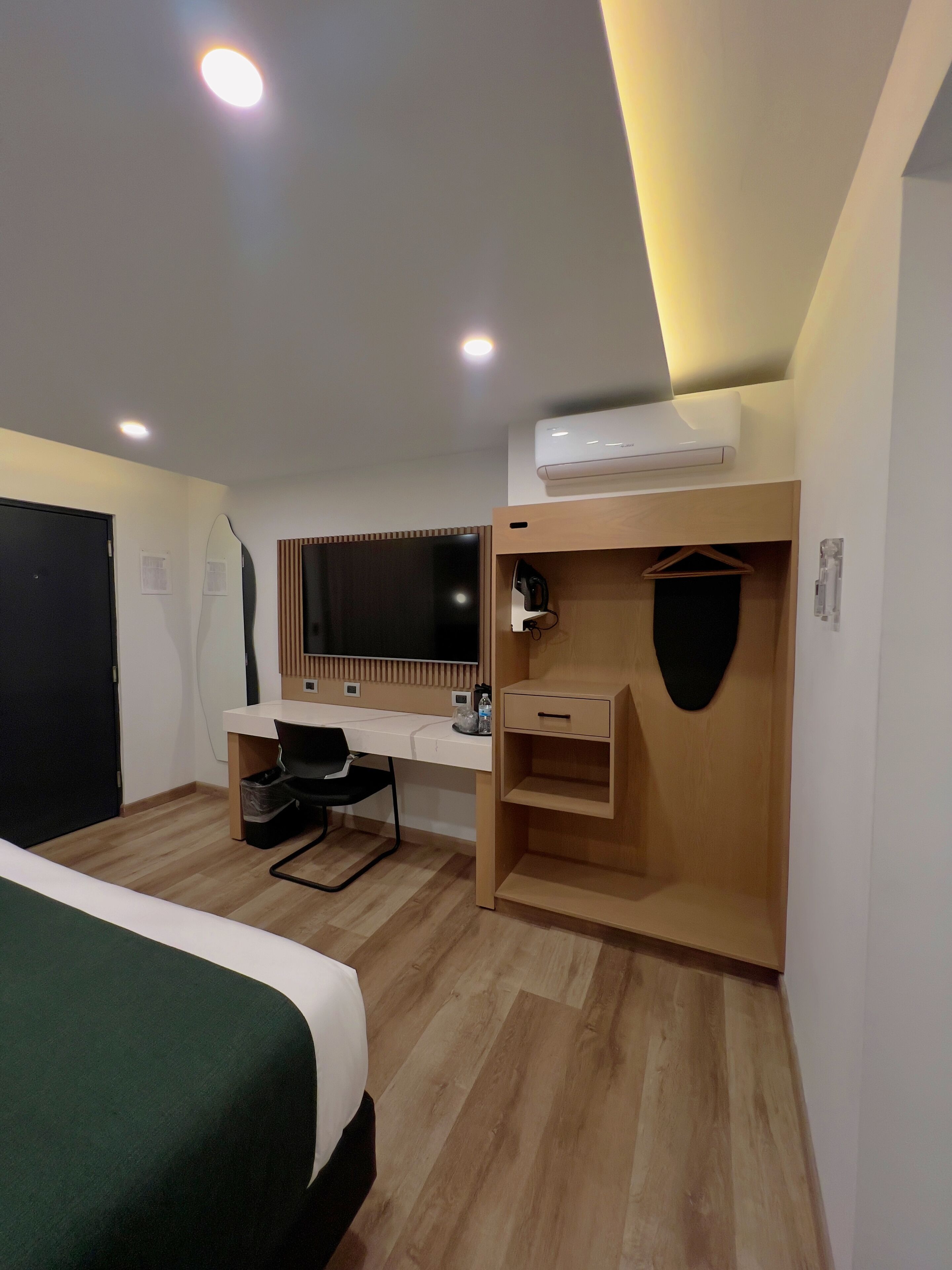 Una habitación de hotel con cama, escritorio, silla, espejo y aire acondicionado.