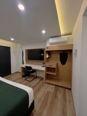 A hotel room with a bed, a desk, a chair, a mirror, and an air conditioning unit. - Hotel Pacific (Tijuana)