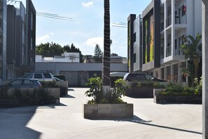 A modern urban street with buildings, parked cars, and a central planter with plants. - Hotel Pacific (Tijuana)
