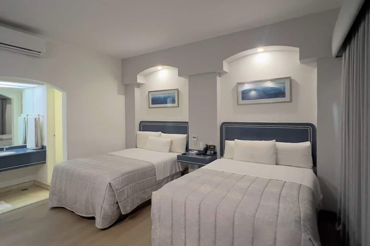 A hotel room with two beds, a bedside table with a phone, and a mirror.