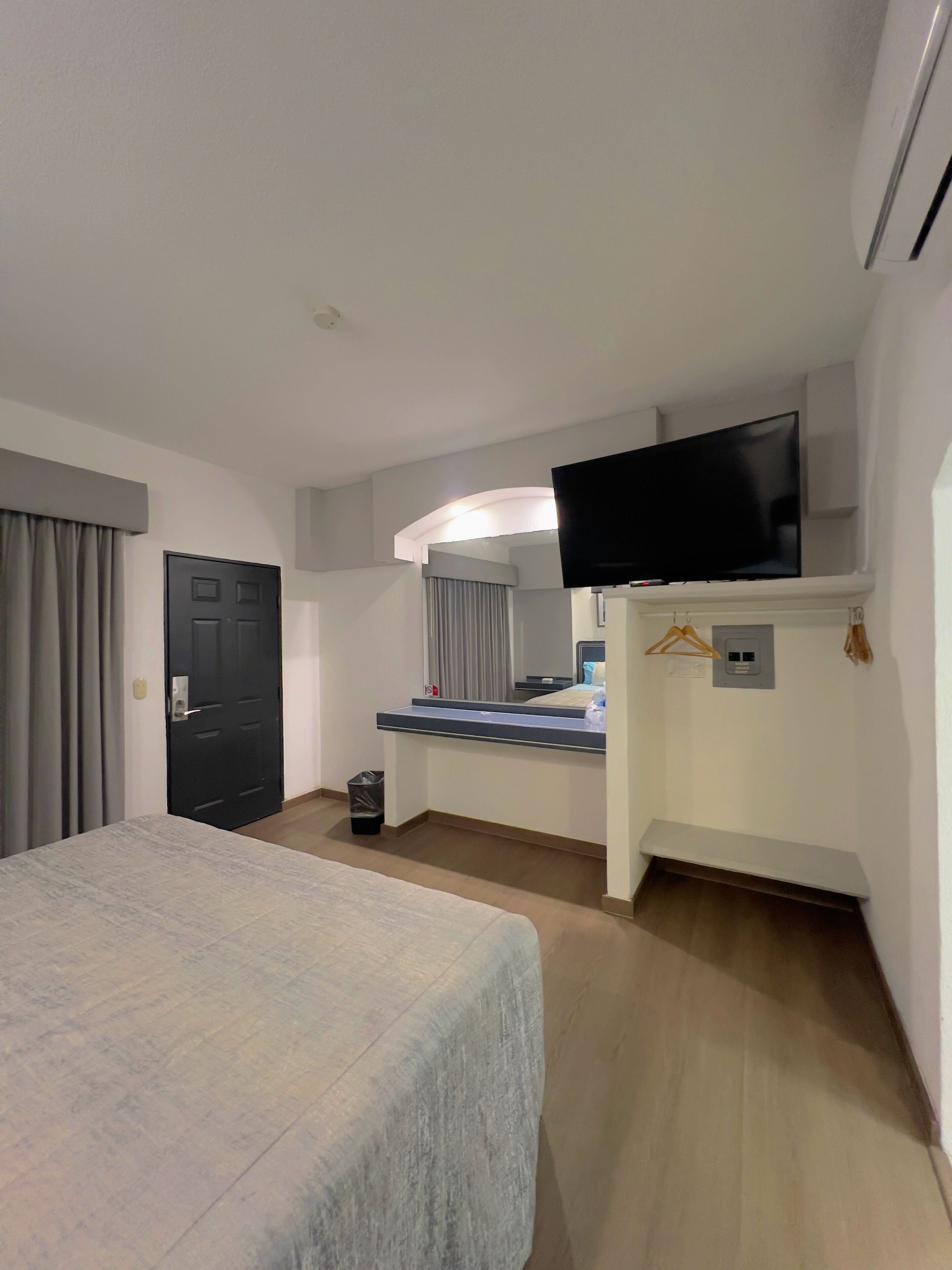 Hotelkamer met een bed, een bureau met een flatscreen televisie, een spiegel en een kleine prullenbak.