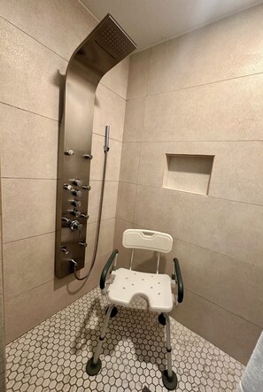 A shower area with a curved showerhead, a handheld shower attachment, and a wheelchair-accessible bench. - Hotel Pacific (Tijuana)