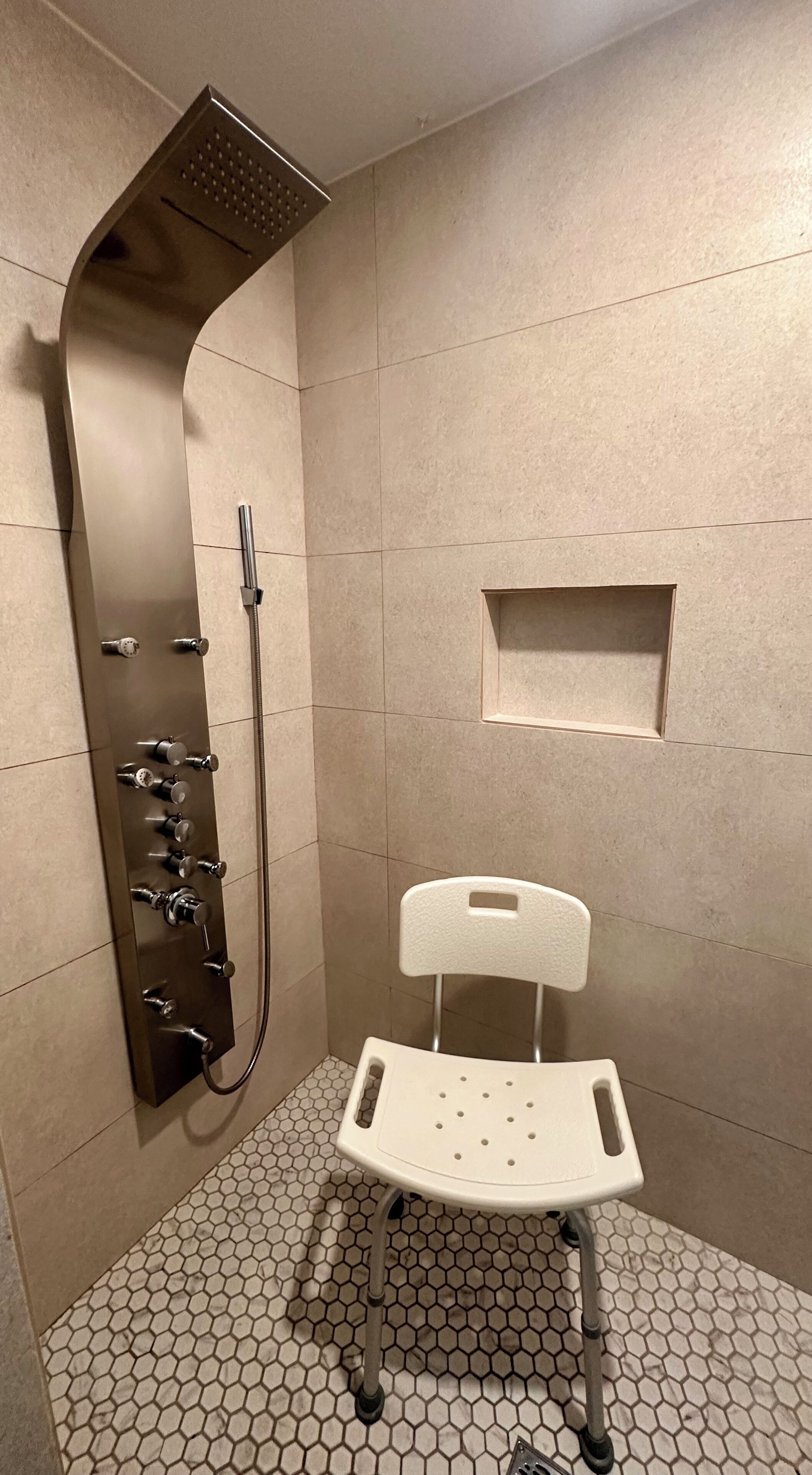 A shower area with a white chair, a wall-mounted showerhead, and a tiled floor.