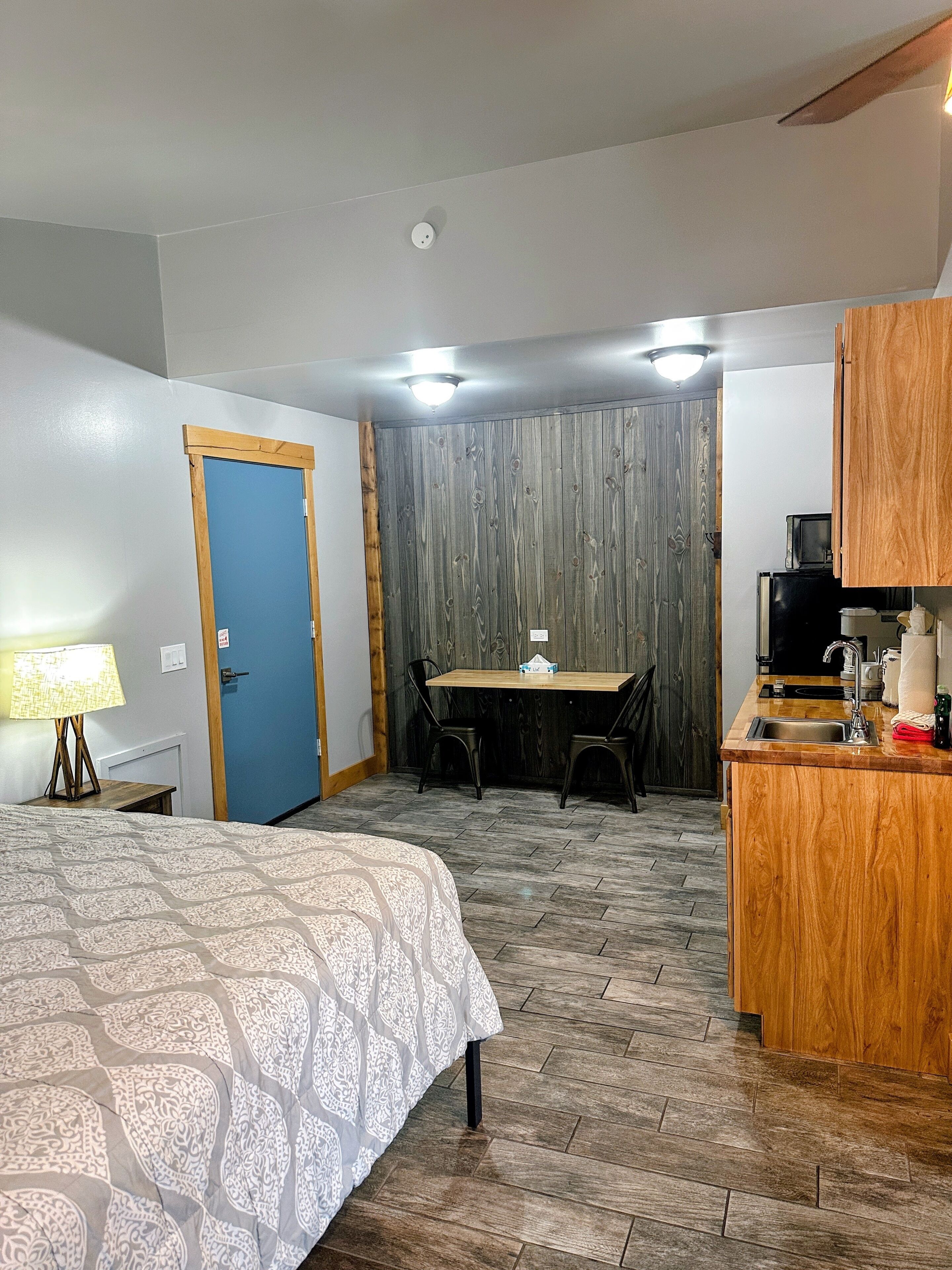Una camera d'albergo compatta con un letto, una piccola scrivania, angolo cottura e una porta blu.