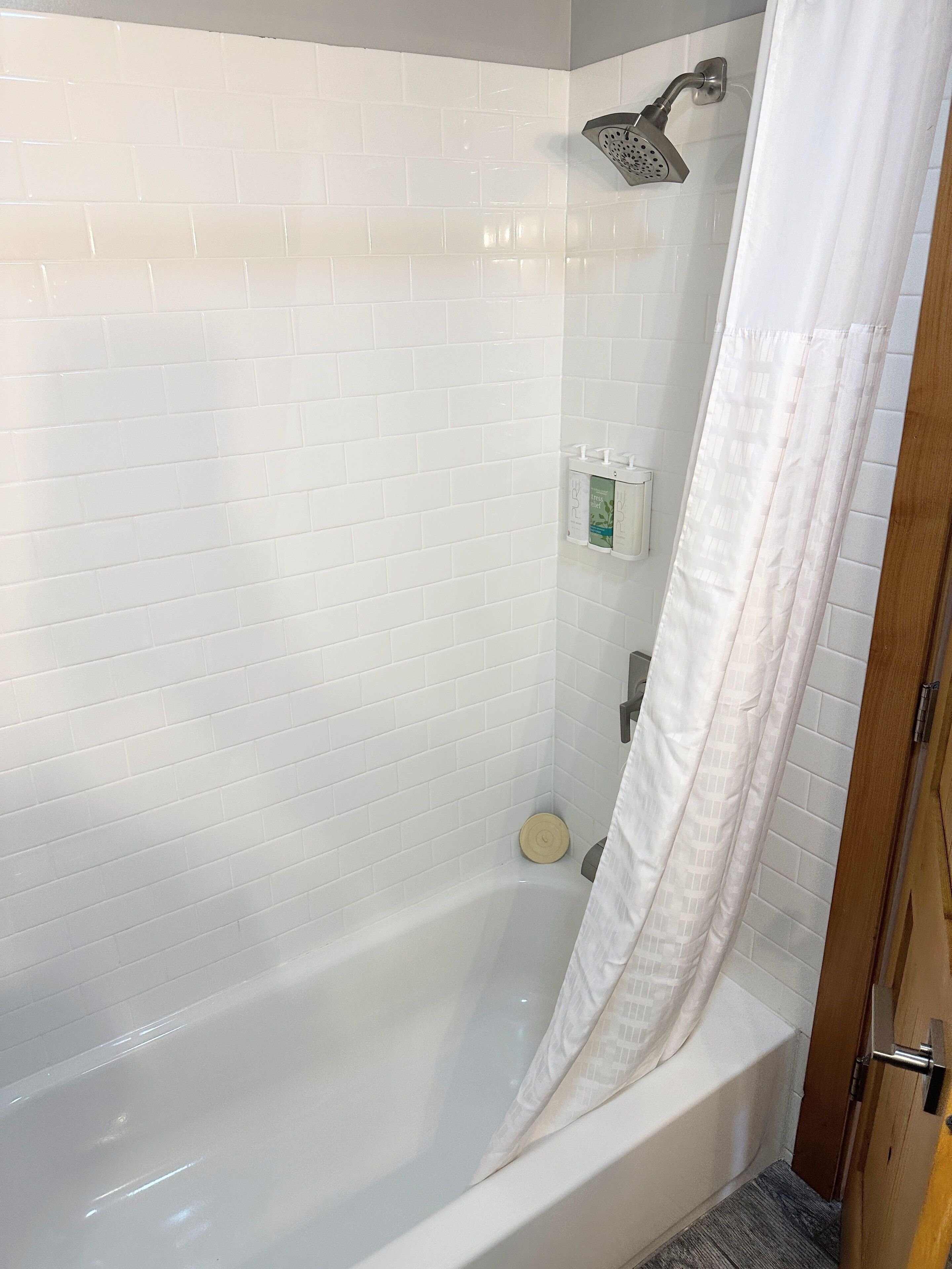A bathroom with a white tiled shower, a white bathtub, and a wooden door.