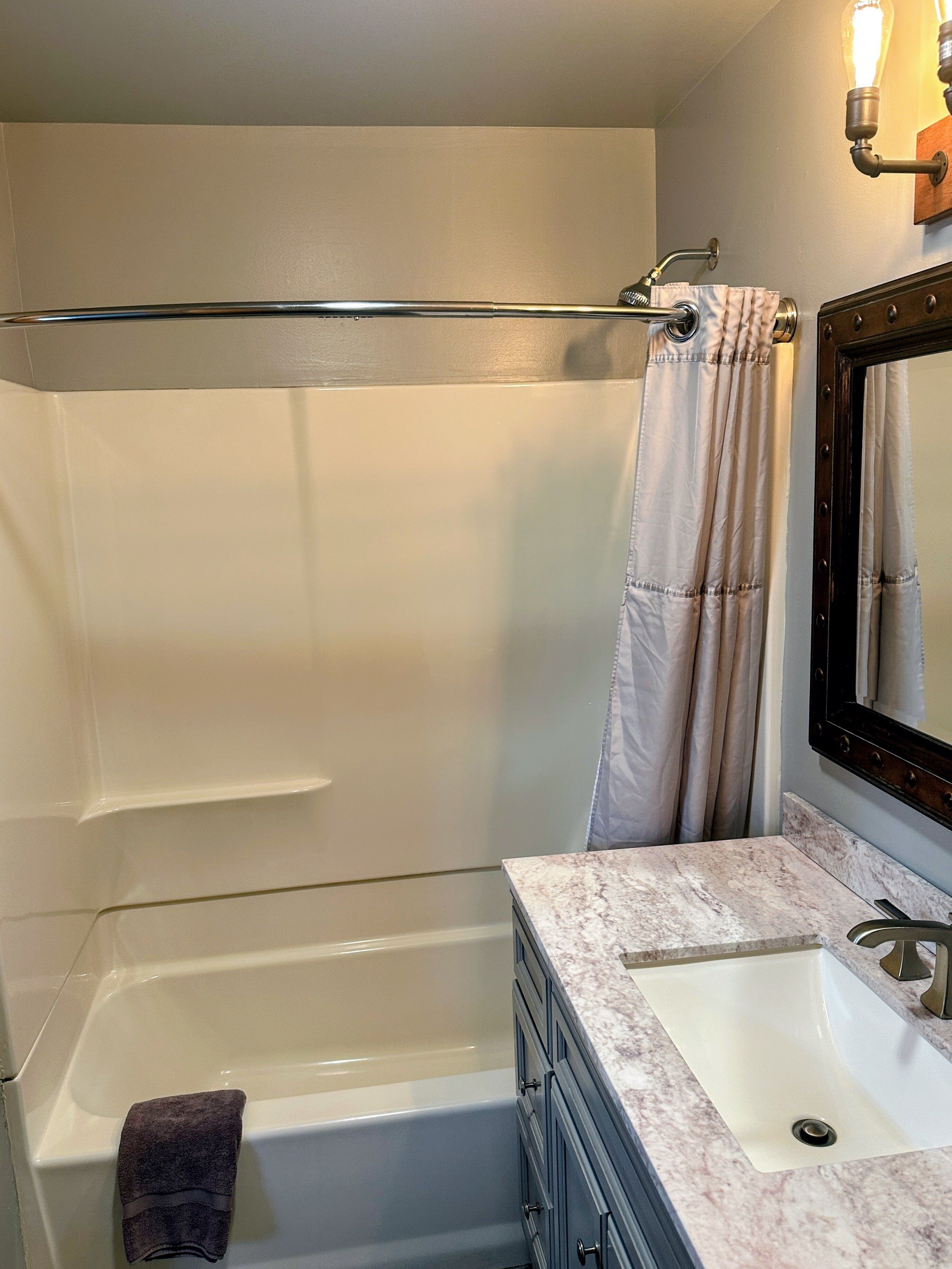 A bathroom with a bathtub, a sink with a marble countertop, a towel rack, and a mirror with a wooden frame.