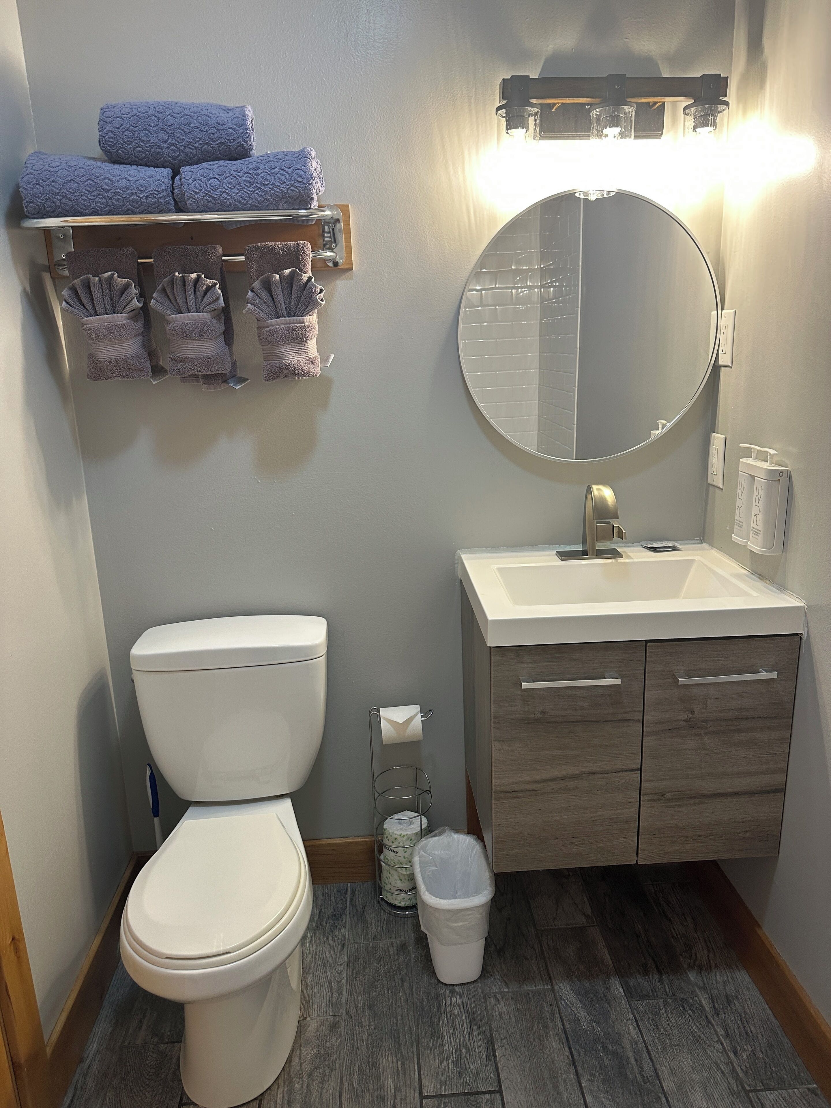 A bathroom with a toilet, sink, mirror, towel rack, and a trash bin.