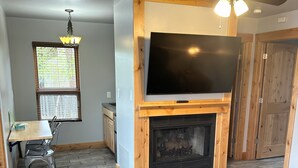 Una sala de estar con chimenea, televisor, ventilador de techo y un comedor con mesa y sillas.