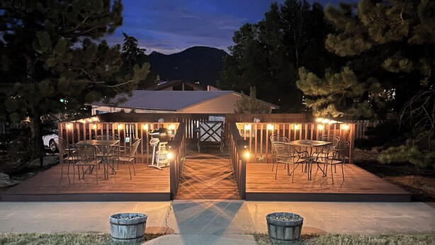 Un patio techado al aire libre con mesas y sillas, una parrilla de barbacoa y una terraza de madera que conduce a un edificio.