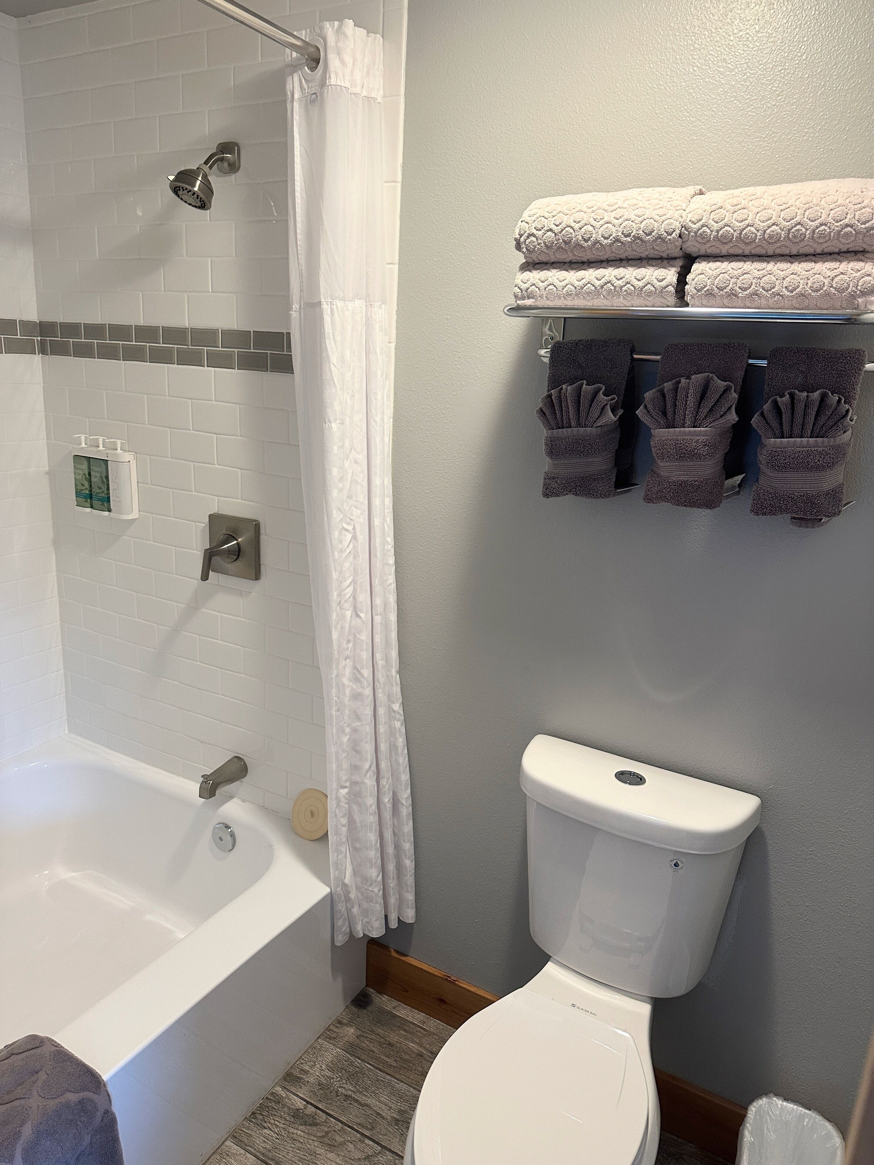 A bathroom with a bathtub, toilet, and towel rack with folded towels.