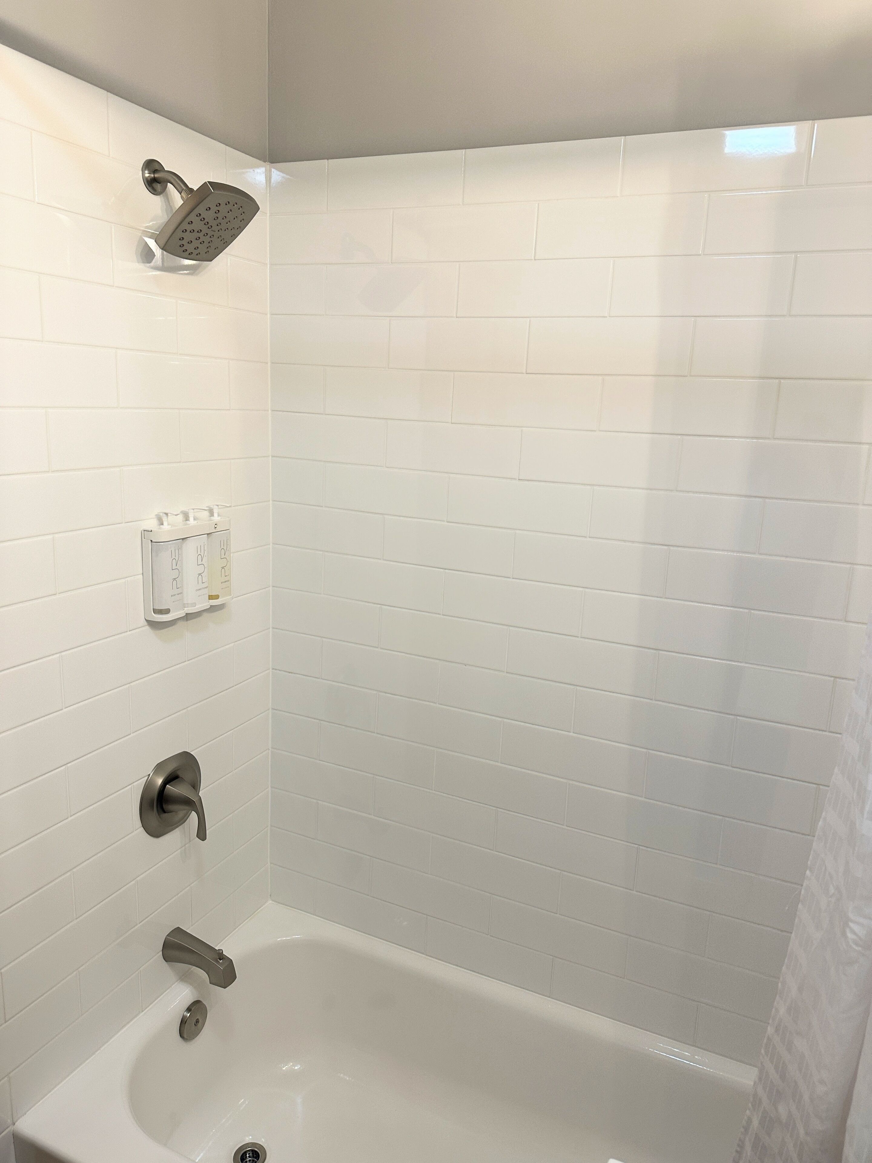 Une salle de bain moderne avec des carreaux de céramique blancs rectangulaires, une pomme de douche, une baignoire et un robinet.