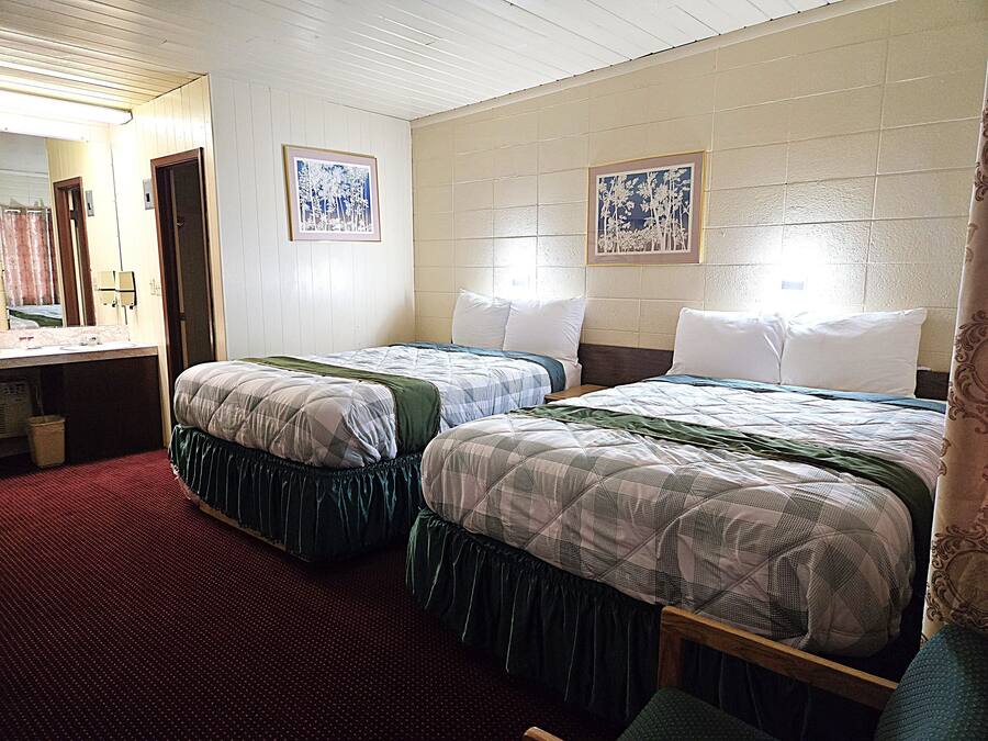 A hotel room with two beds, a bathroom, and a mirror.