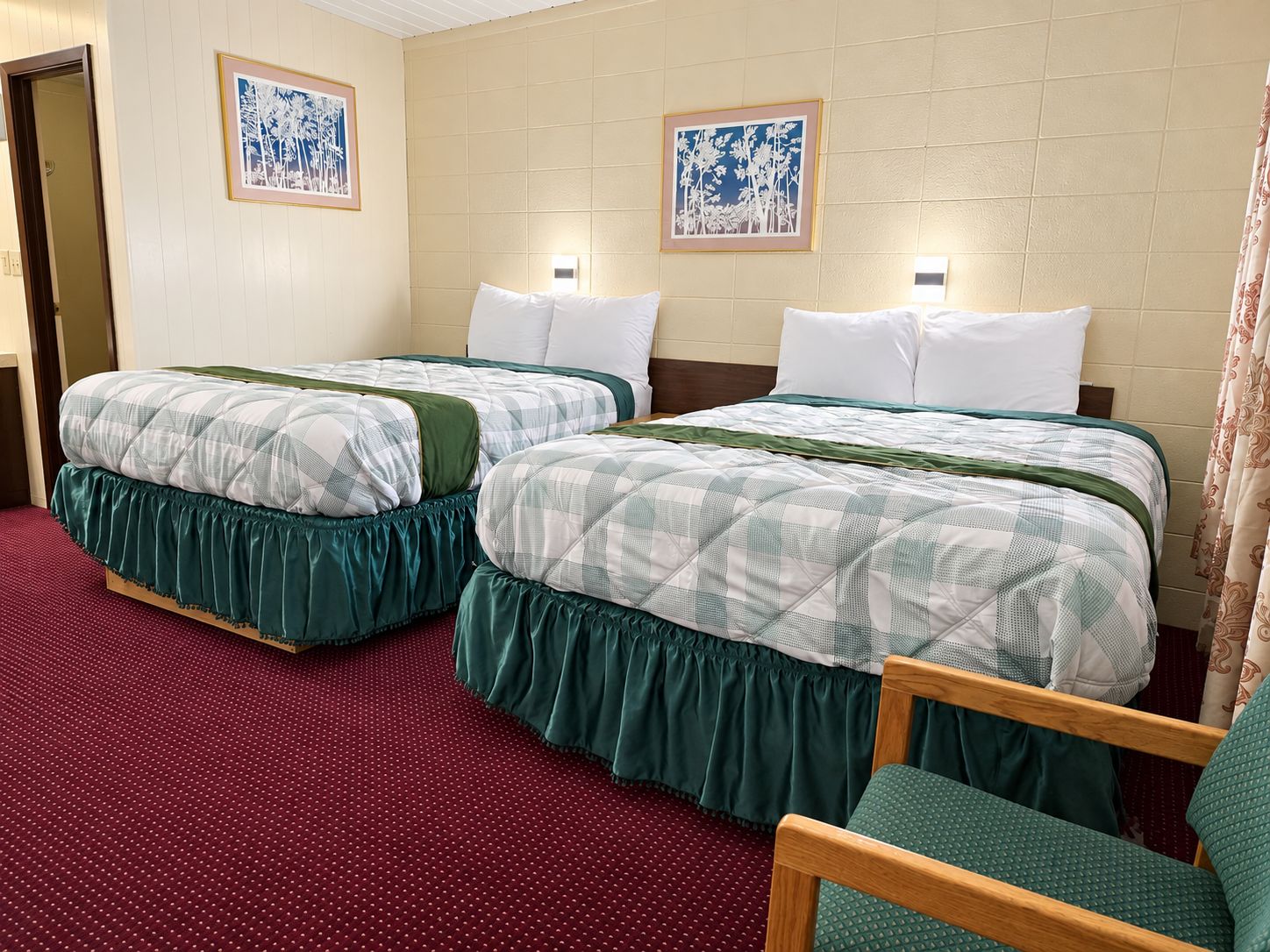 Habitación de hotel con dos camas, alfombra roja, cabeceros de madera y dos obras de arte enmarcadas.
