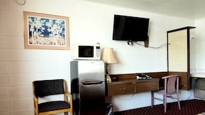 A compact hotel room with a bed, a refrigerator, a microwave, a television, a desk with a chair, and a wall-mounted TV. - Town House Motor Inn (Worland)