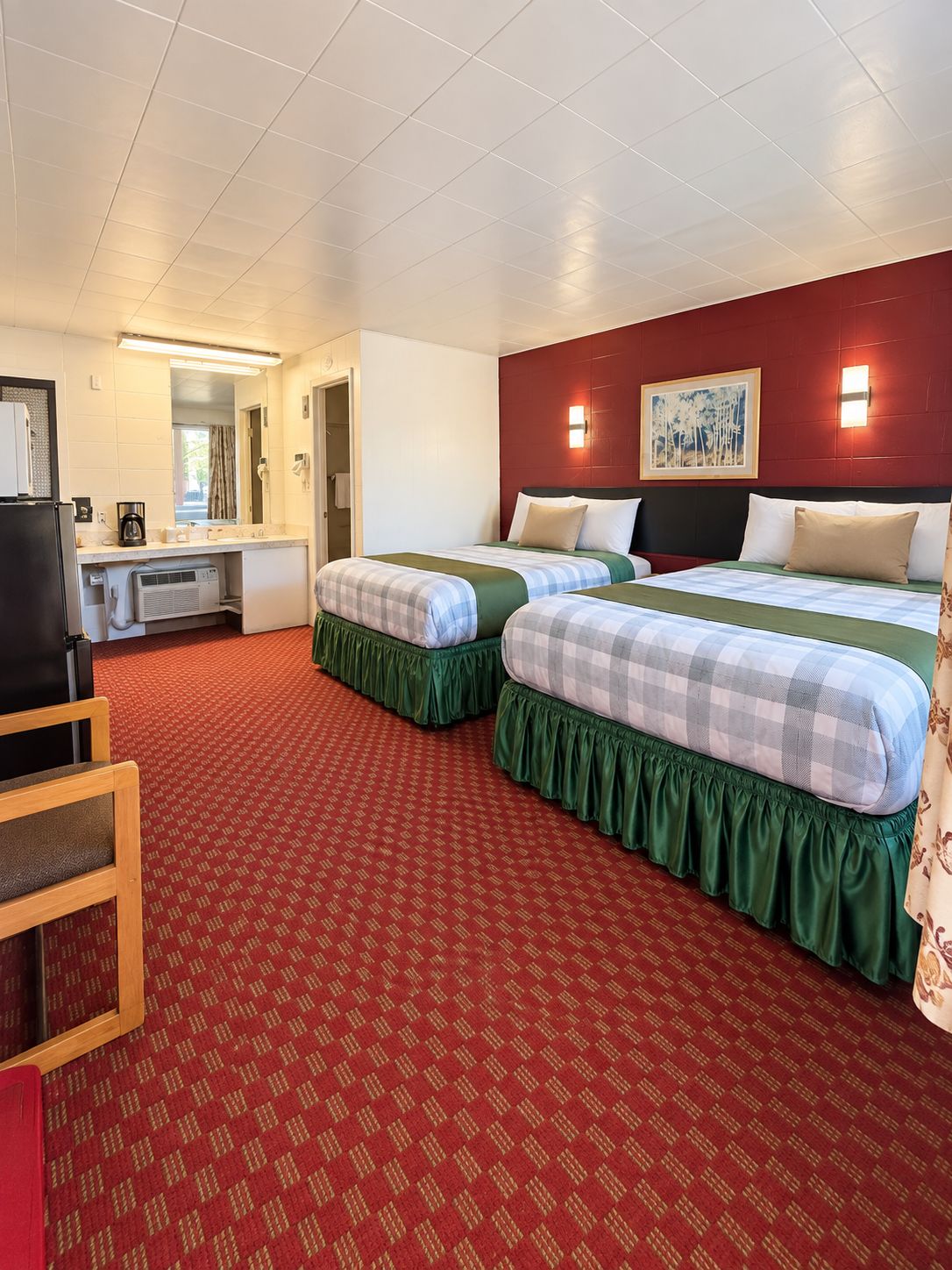 A hotel room with two beds, a desk, and a kitchenette.