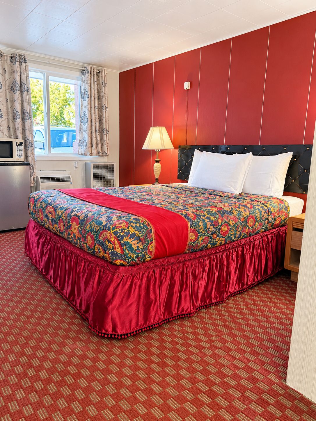 A hotel room with a large bed, a bedside lamp, a microwave, and a window with curtains.