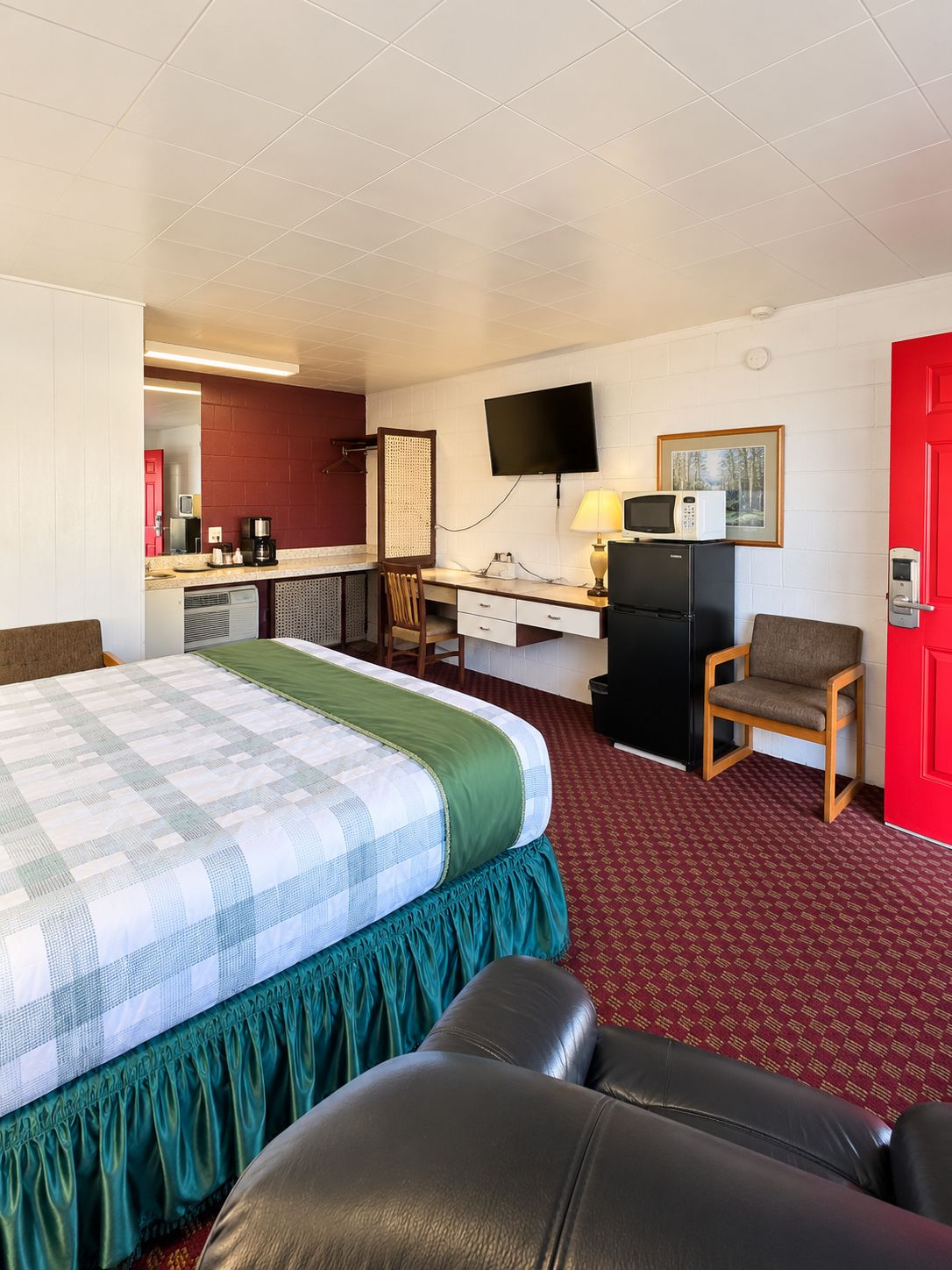Ett hotellrum med en säng, ett skrivbord med en dator, en stol, en tv och en röd dörr.
