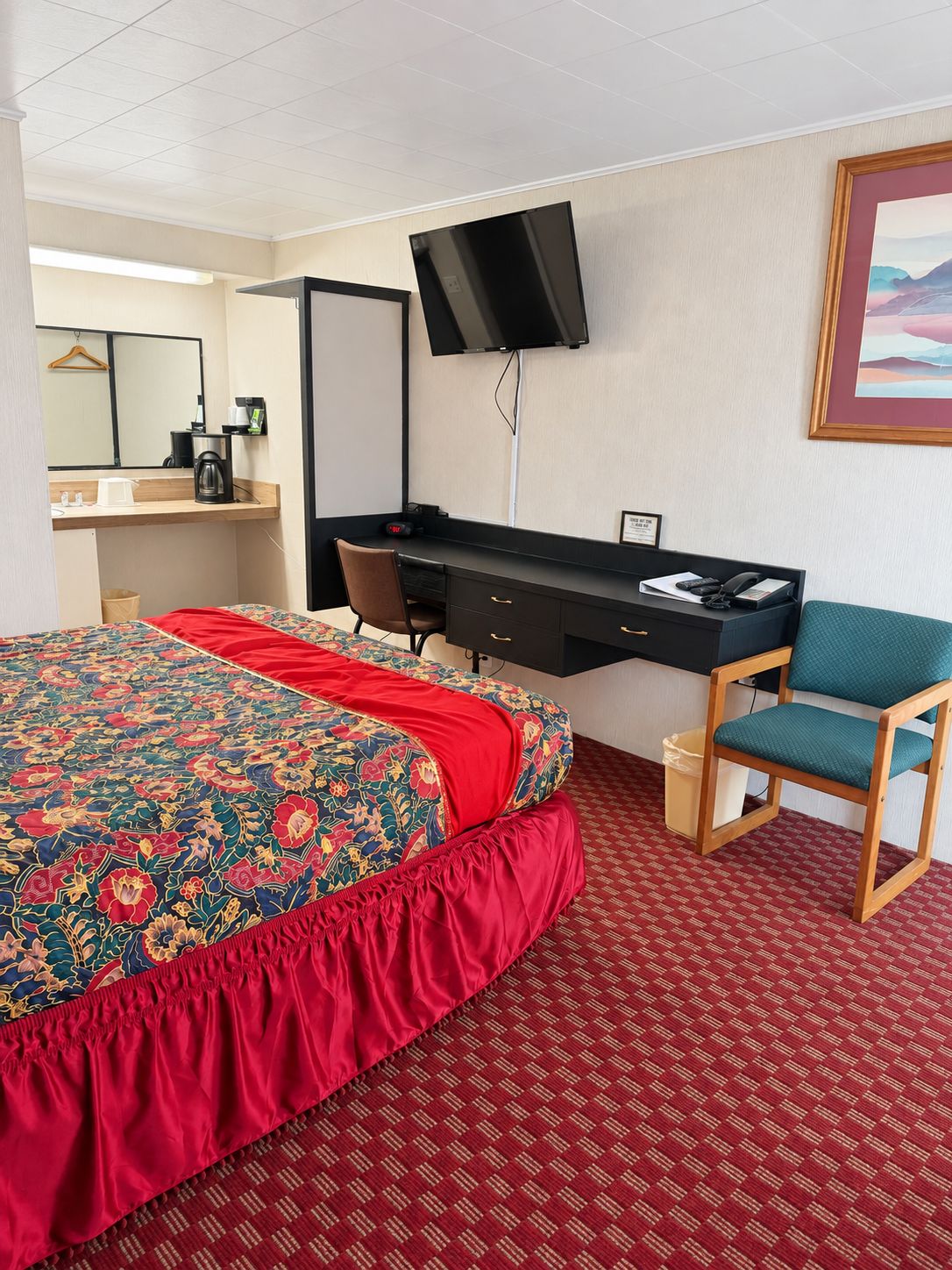 Una habitación de hotel con una cama, un escritorio con silla, un televisor y un cuadro en la pared.