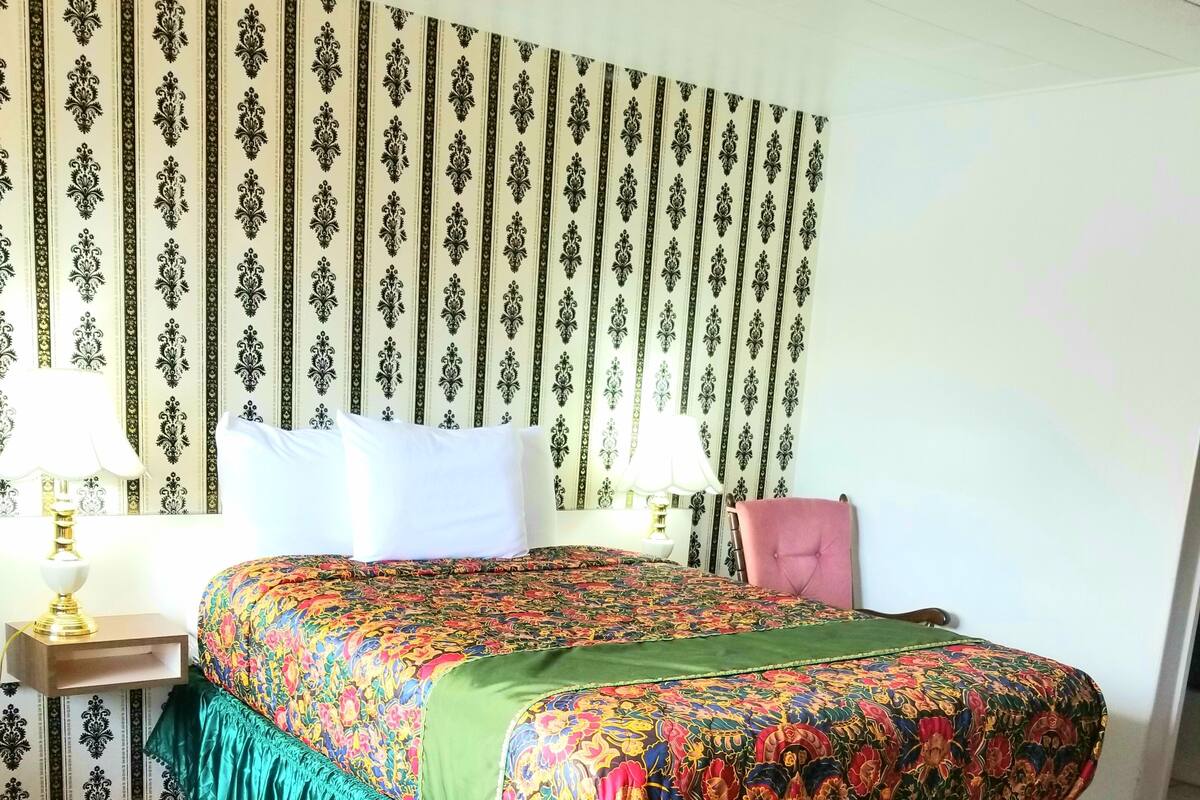 Une chambre d’hôtel avec un grand lit, deux tables de chevet, une chaise et un papier peint à motifs.