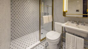 Un baño con inodoro blanco, lavamanos y zona de ducha con puerta de cristal.