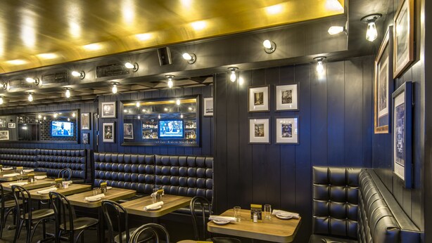 Un interior de restaurante con cabinas, mesas y una zona de bar.