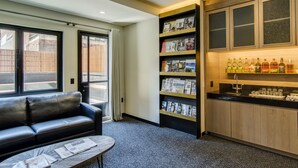 Una habitación de hotel moderna con un sofá de cuero, una mesa de centro con revistas, una estantería con revistas y un minibár con botellas de licor.