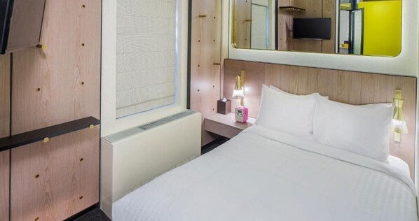 A hotel room with a bed, bedside table, lamp, and a mirror.
