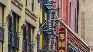 Un edificio histórico con un llamativo letrero de 'HOTEL SHOCARD', un letrero de 'Gleasons Tavern' y un letrero que anuncia 'Strictly Limited Engagements'.