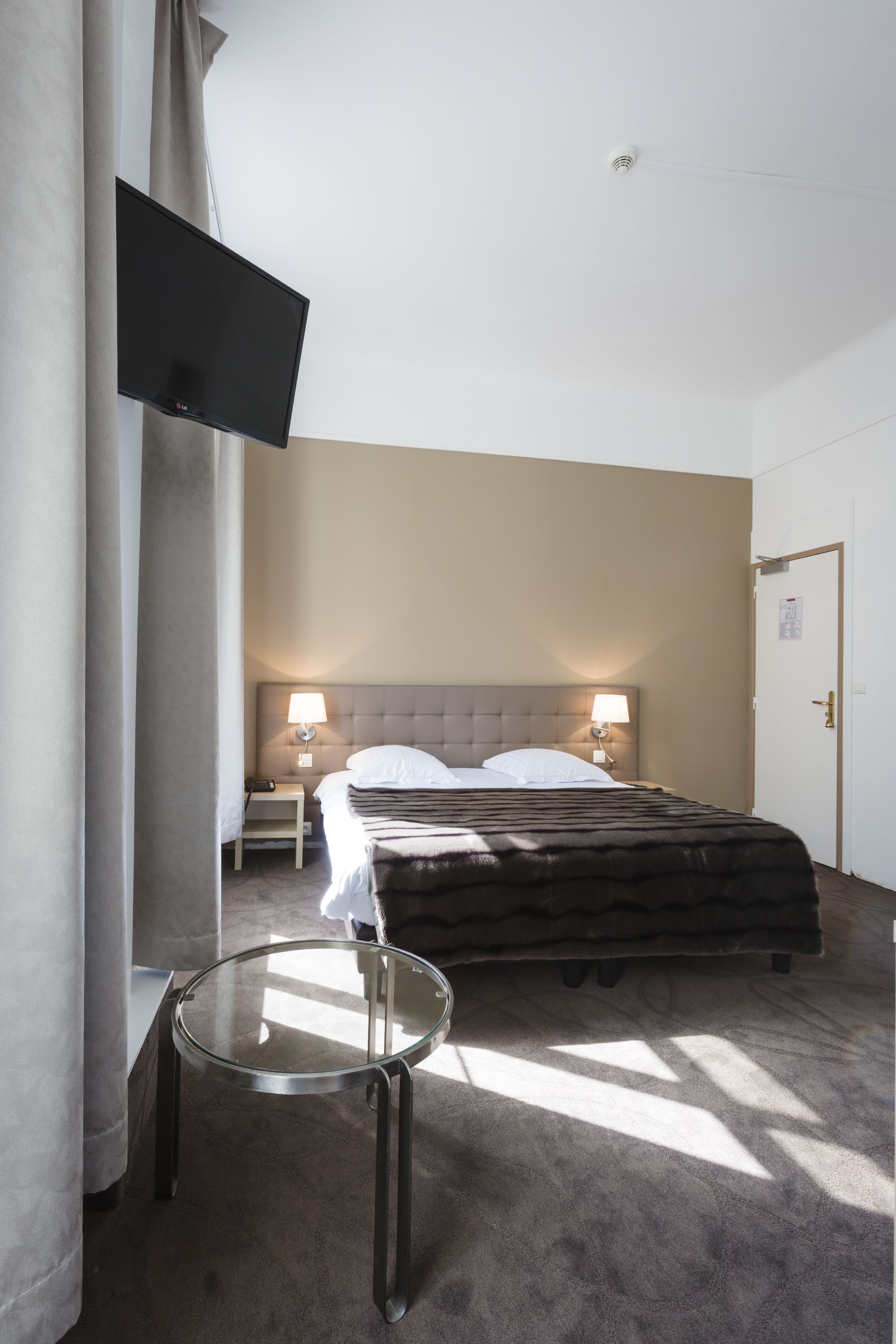 Habitación de hotel con cama, lámparas de noche, televisor de pantalla plana en la pared y una mesa redonda de cristal.