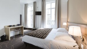Een hotelkamer met een bed, een bureau, een stoel, een televisie en een raam met gordijnen.