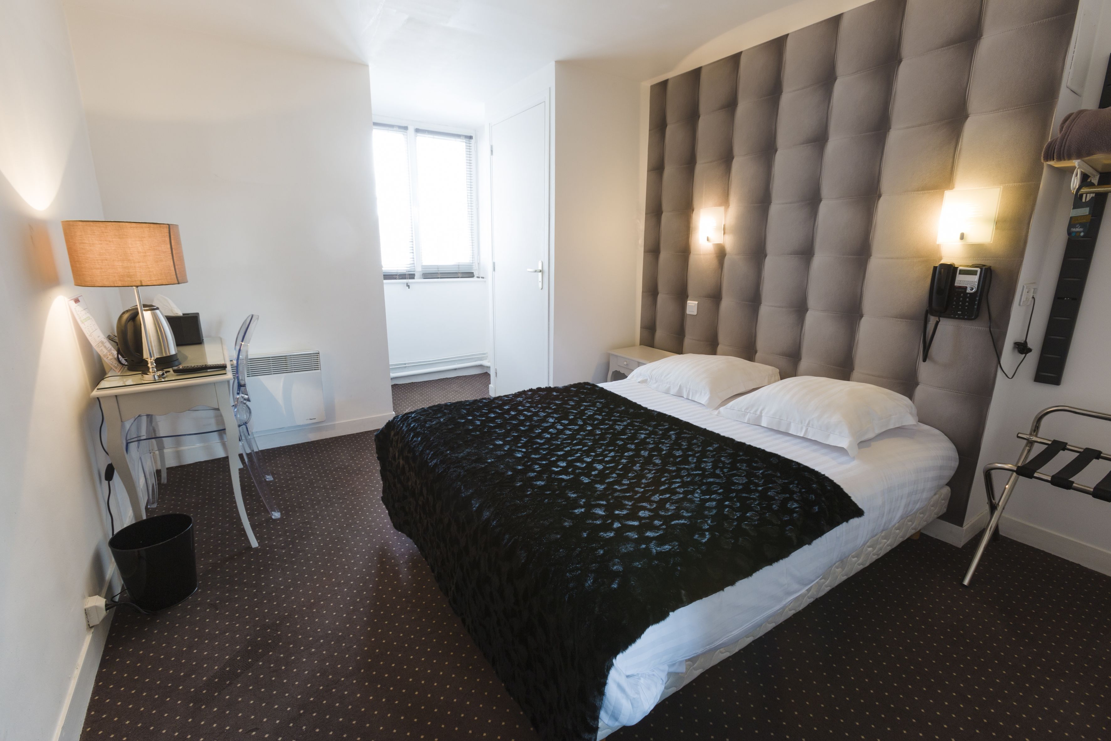 A modern hotel room with a large bed, a desk with a lamp, and a phone on the wall.