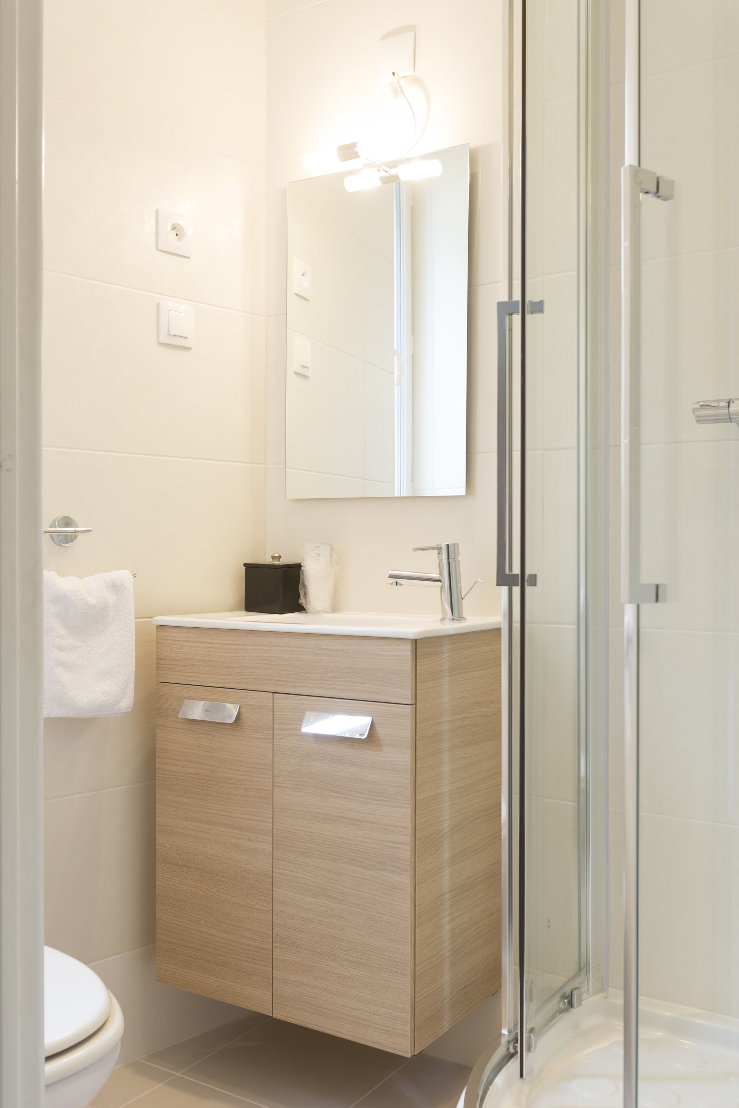 A modern bathroom with a glass shower enclosure, a wooden vanity, and a white toilet.