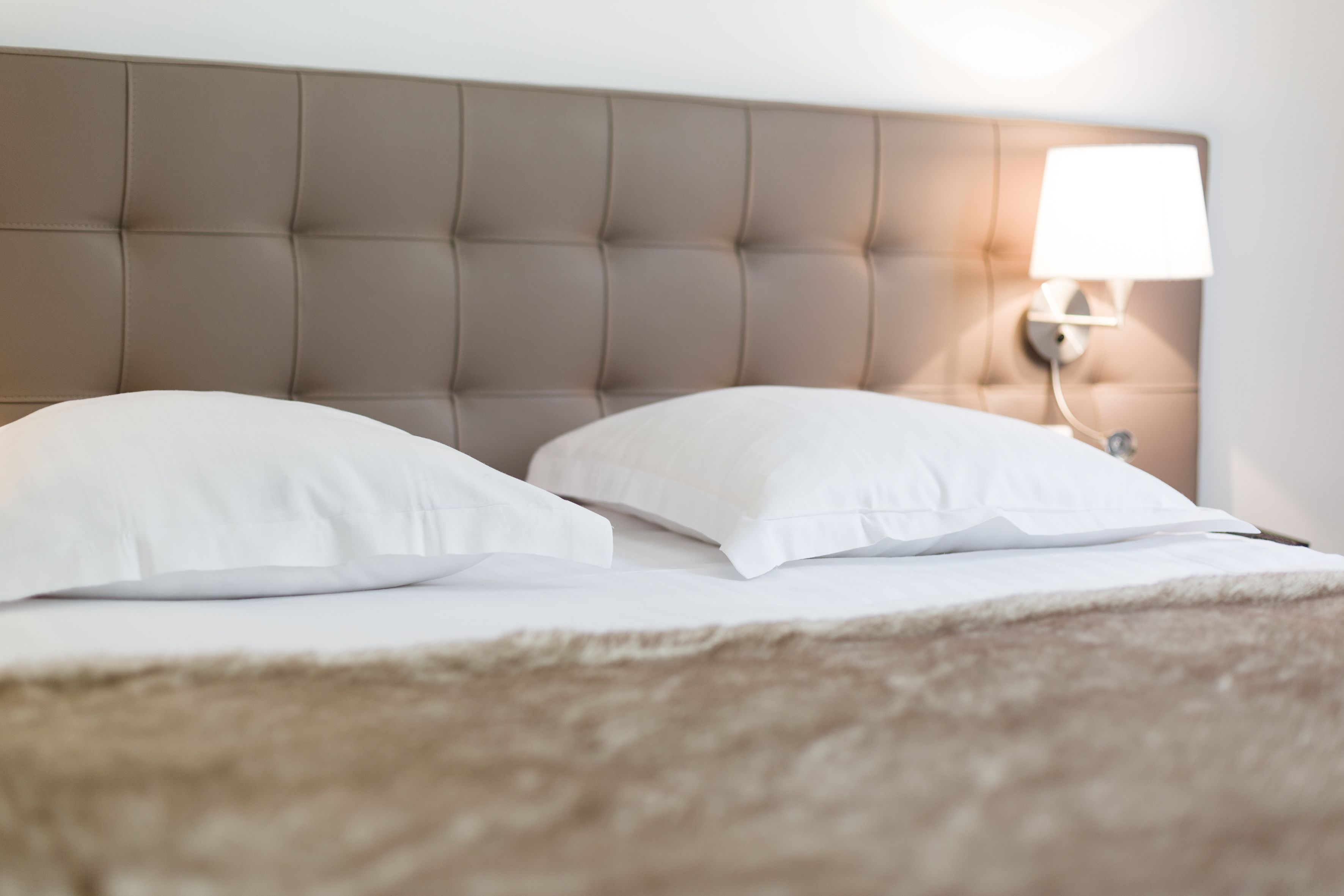 Een net opgemaakt bed met een gestoffeerd hoofdbord en een bedlampje.