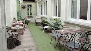 Een gezellig buitenterras met houten meubels, plantenpotten en een gazon van kunstgras.
