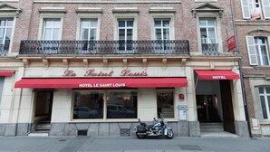 Een hotelgevel met een rode luifel, meerdere ramen en een motorfiets ervoor geparkeerd.