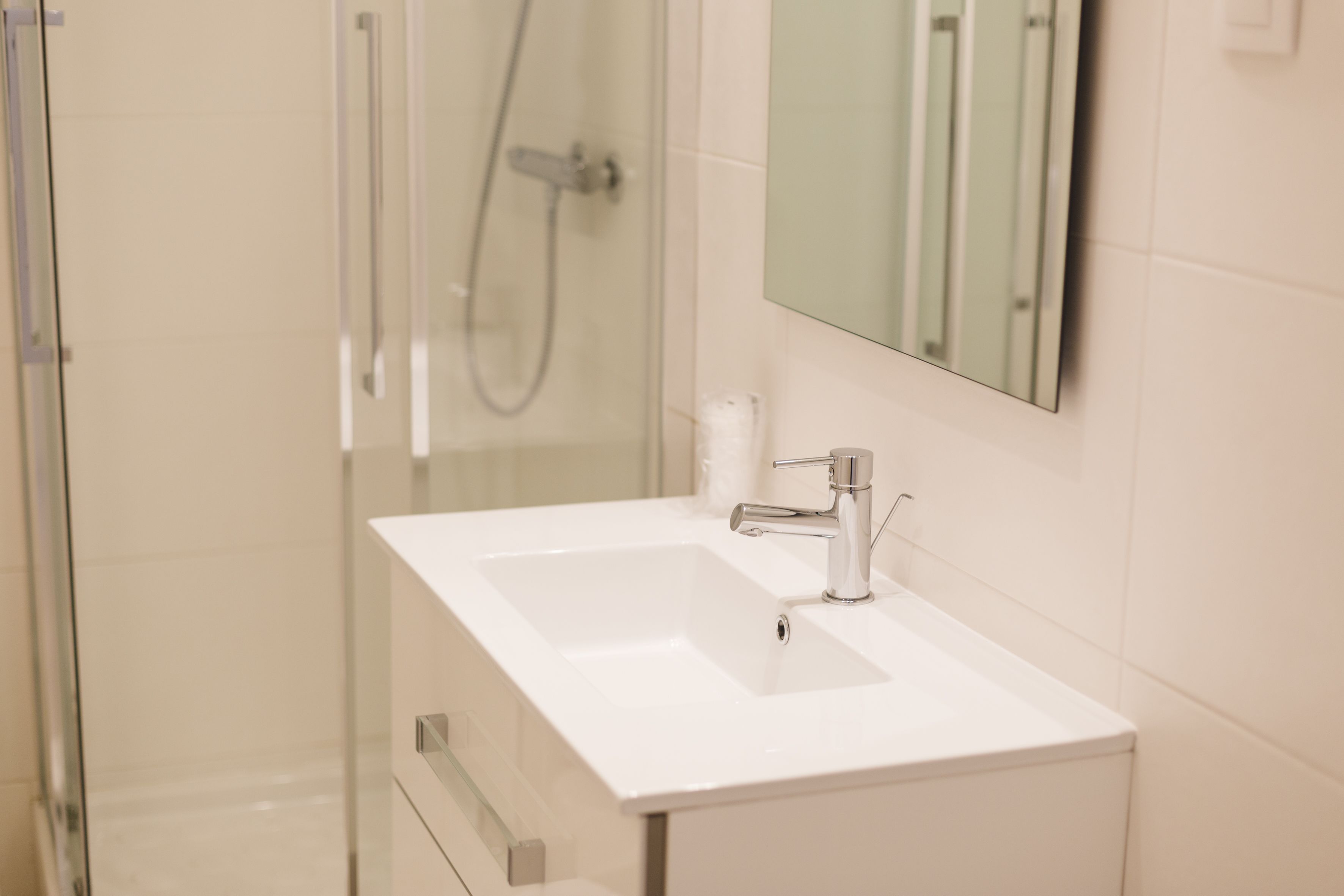 Un baño con lavamanos blanco, un espejo y zona de ducha.
