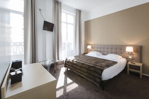 Habitación de hotel con cama, lámparas de noche, escritorio con silla y televisor en la pared.