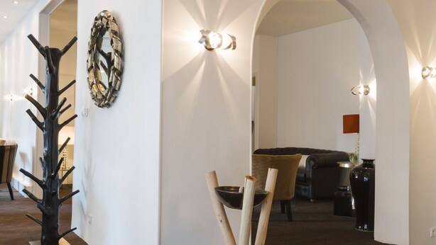 Een modern interieur met een trap die leidt naar een eethoek, een houten sculptuur en een wandlamp.