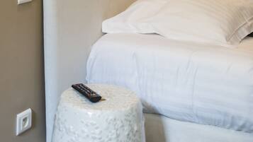 A neatly made bed with white bedding, a remote control on a round stool, and wall-mounted light fixtures.