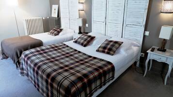A hotel room with two beds, each with a plaid bedspread, a bedside table with a lamp, and a wall-mounted light fixture.